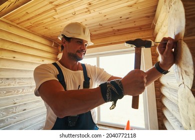 Housebuilder Driving A Nail Into Log Of House Wall