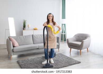 Housecleaning Service. Happy Young Maid With Vacuum Cleaner Standing In Middle Of Tidy Living Room, Full Length Portrait. Positive Millennial Housewife Doing Domestic Chores, Copy Space