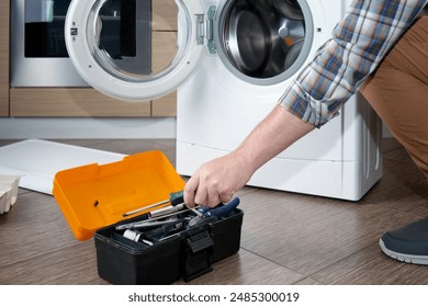 A household appliance repairman disassembling a washing machine with a screwdriver. Professional repair of household appliances.