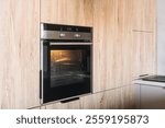 Household appliances. Modern kitchen displays contemporary design elements with a black oven seamlessly integrated into wooden cabinetry, showcasing a stylish and efficient cooking space.