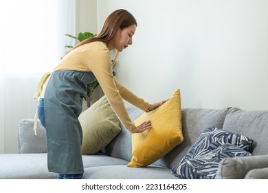 Household clean up, housekeeper asian young woman, girl cleaning, hand keeping put pillow on sofa, couch in living room at home. Messy maid or housewife organizing dirty and untidy. Chore concept.