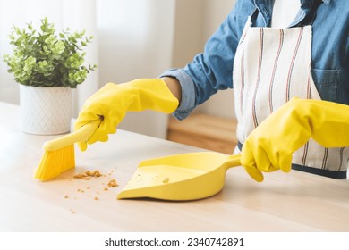 Household clean up, housekeeper asian young woman wearing protection rubber yellow gloves, using broom, dustpan sweeping remove spilled crumb food broken on dirty table at home, equipment for cleaning - Powered by Shutterstock