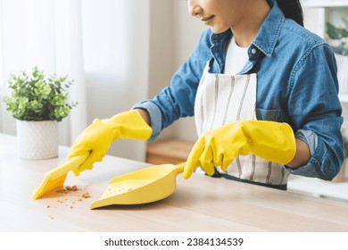 Household clean up, housekeeper asian young woman wearing protection rubber yellow gloves, using broom, dustpan sweeping remove spilled crumb food broken on dirty table at home, equipment for cleaning - Powered by Shutterstock