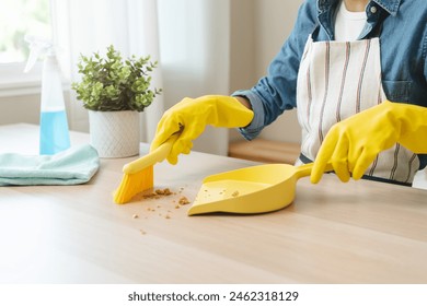 Household clean up, housekeeper asian young woman wearing protection rubber yellow gloves, using broom, dustpan sweeping remove spilled crumb food broken on dirty table at home, equipment for cleaning - Powered by Shutterstock