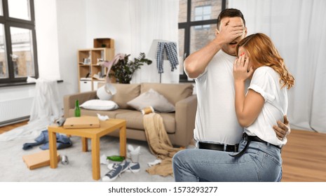 Household, Cleaning And Domestic Life Concept - Scared Couple In White T-shirts Over Messy Home Room Background