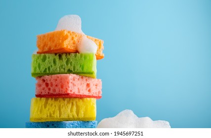 Household Cleaning Scrub Colored Sponges with soap foam. Kitchen Dishwashing Sponge on blue background. Cleaning home concept. Space for text.