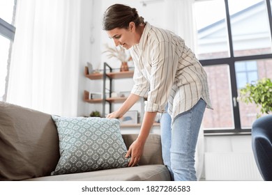 household, home improvement and cleaning concept - happy smiling woman arranging cushions on armchair and sofa