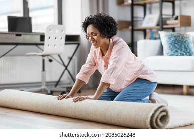 household, home improvement and interior concept - happy smiling young woman unfolding carpet on floor