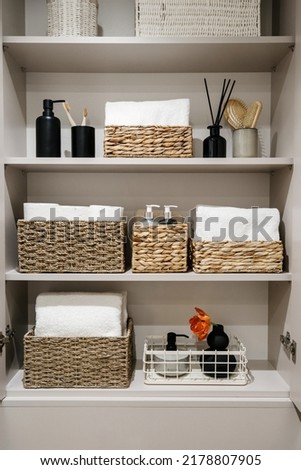 Household items, toilet paper rolls, white bath towels and cosmetics bottles on shelves in the bathroom cabinet Organization of space in wardrobe. Bedding, linen, home perfumes and folded bathrobes