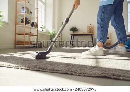 Household service with a close up of a woman dedicated to cleaning the house through vacuuming. She expertly maneuvers the vacuum over the living room carpet, conveying a well maintained home floor.