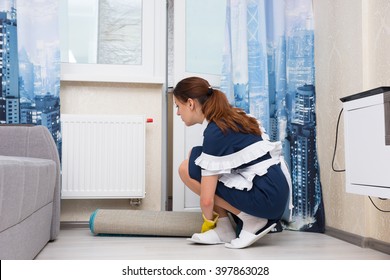 Housekeeper crouching down and checking the thermostat on a radiator as she cleans in a living room or hotel suite