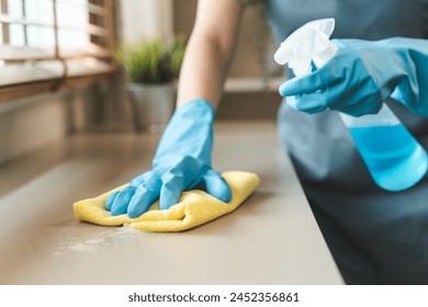 Housekeeper doing chores concept, Close-Up view of housemaid cleaning furniture surface with sanitizer spray and wiping with wet cloth in living room. - Powered by Shutterstock