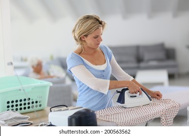 Housekeeper At Home Ironing Clothes For Old Woman