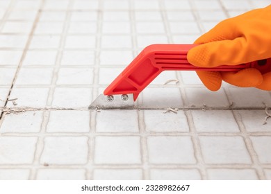 Housekeeper remove old grout from bathroom tiles.  Raking out grout tiles for regrouting.