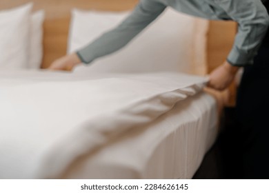 A housekeeper in a uniform makes a bed preparing luxury hotel room for guests cleaning and travel concept - Shutterstock ID 2284626145