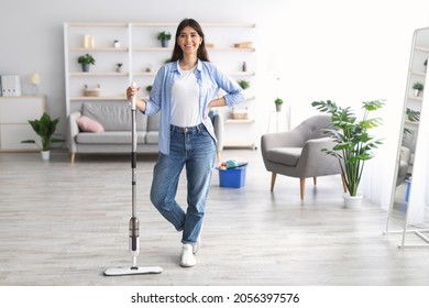Housekeeping Job Concept. Smiling young woman in casual clothes washing wooden laminate floor using modern mop, doing homework cleaning routine, happy lady posing and looking at camera