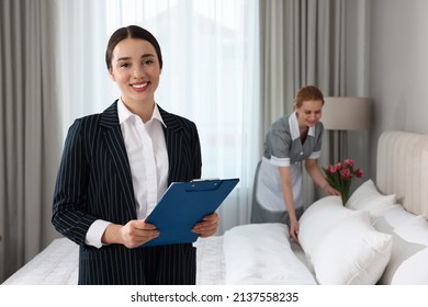 Housekeeping Manager With Clipboard Checking Maid's Work In Hotel Bedroom