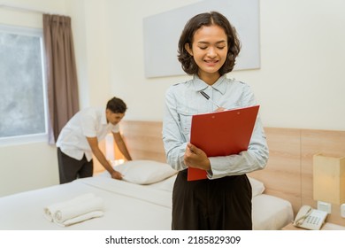 Housekeeping Manager Writing Clipboard Notes On Maid Cleaning Hotel Room Background