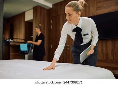 Housekeeping supervisor checking bed made by room attendant in hotel room. Copy space.