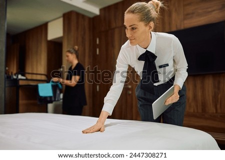 Housekeeping supervisor checking bed made by room attendant in hotel room. Copy space.