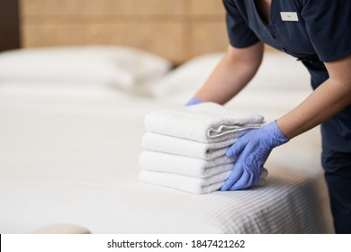 Housemaid making bed in hotel room while folding towels - Shutterstock ID 1847421262