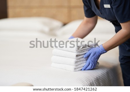 Housemaid making bed in hotel room while folding towels