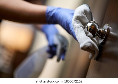 Housemaid in protective gloves disinfecting the door handle in hotel