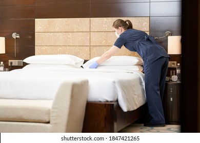 Housemaid standing near bed while cleaning the room in hotel