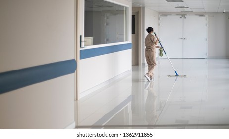 Housemaid Using The Mop In Hospital Walkway To Cleaning The White Floor With Reflection. 