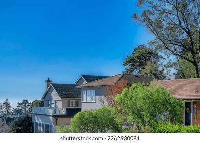 Houses amid blue sky and trees in San Francisco Califronia residential area. Gable roof, balcony, panelled wall and brick wall can be seen at the facade of the beautiful homes.