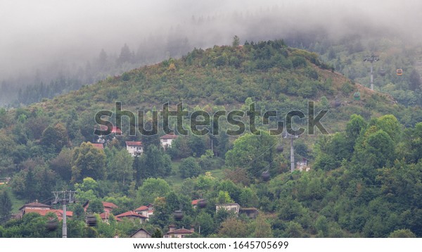 Houses on a hill with cable car moving up and\
down from Sarajevo station to mountains, Bosnia And Herzegovina.\
Houses with red roofs and green\
trees