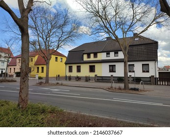 Houses on one of the streets of the residential area of Keten. On the right is a house in yellow and white tones with a dark roof. To the left is a lemon-beige house with a red roof. Germany