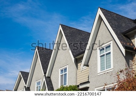 Houses with shingle roof against blue sky. Edge of roof shingles on top of the houses dark asphalt tiles on the roof. Nobody, street photo, selective focus