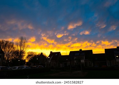 Houses are silhouetted against a colourful display of mammatus clouds at sunset - Powered by Shutterstock