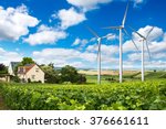 Houses with solar panels on roof and wind turbines nearby. Summer landscape with green vineyard. Eco energy concept.