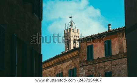 houses in a street in siena in Italy, showing part of a church bell tower.