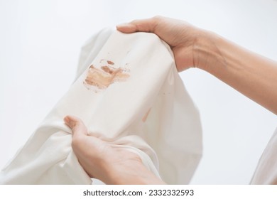 Housewife, asian young maid woman hand in holding white shirt, showing making cloth stain, spot dirty or smudge on clothes, dirt stains for cleaning before washing, making household working at home. - Shutterstock ID 2332332593