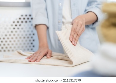 Housewife, Asian Young Woman Hand In Many Folding Freshly Shirts, Sweaters Or Dress On Desk, Table After Washing Clean Clothes And Drying, Making Household Working In Room At Home. Laundry And Maid.