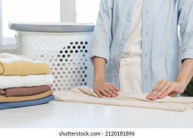 Housewife, Asian Young Woman Hand In Many Folding Freshly Shirts, Sweaters Or Dress On Desk, Table After Washing Clean Clothes And Drying, Making Household Working In Room At Home. Laundry And Maid.