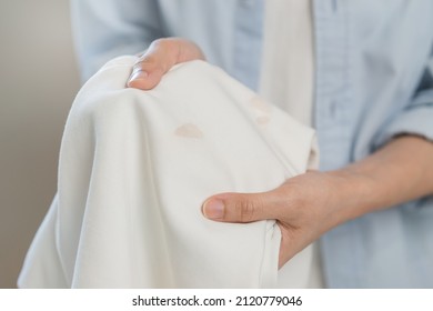 Housewife, asian young woman hand in holding shirt, showing making stain, spot dirty or smudge on clothes, dirt stains for cleaning before washing, making household working at home. Laundry and maid. - Shutterstock ID 2120779046