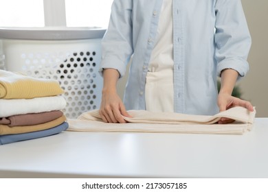 Housewife, Asian Young Woman Hand In Many Folding Freshly Shirts, Sweaters Or Dress On Desk, Table After Washing Clean Clothes And Drying, Making Household Working In Room At Home. Laundry And Maid.