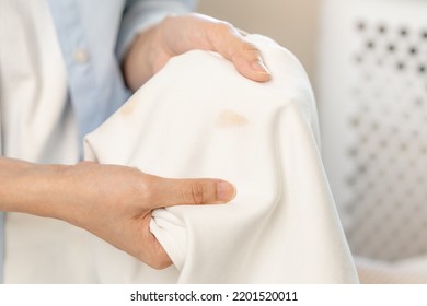 Housewife, asian young woman hand in holding shirt, showing making stain, spot dirty or smudge on clothes, dirt stains for cleaning before washing, making household working at home. Laundry and maid. - Shutterstock ID 2201520011