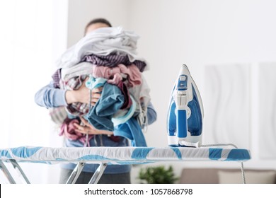 Housewife bringing a huge pile of laundry on the ironing board, boring household chores concept
