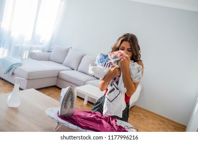 Housewife Bringing A Huge Pile Of Laundry On The Ironing Board, Boring Household Chores Concept. Disappointed Unhappy Housewife. Sad Woman Ironing Clothing At Home