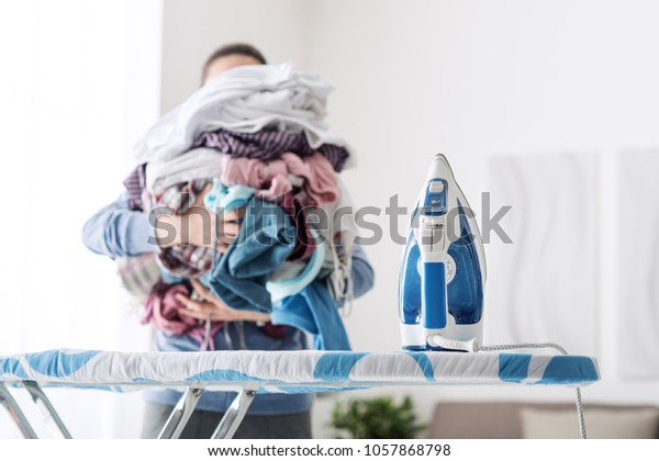 Housewife bringing a huge pile\
of laundry on the ironing board, boring household chores\
concept