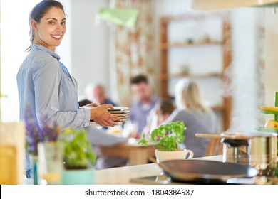 Housewife Cleaning Dishes In Kitchen With Family In Background