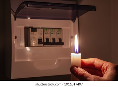 Housewife in complete darkness holding a candle to investigate a home fuse box during a power outage. Blackout, symbolic image.