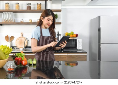 The housewife dressed in an apron  using tablet computer to find recipes on the internet. Morning atmosphere in a modern kitchen. - Powered by Shutterstock