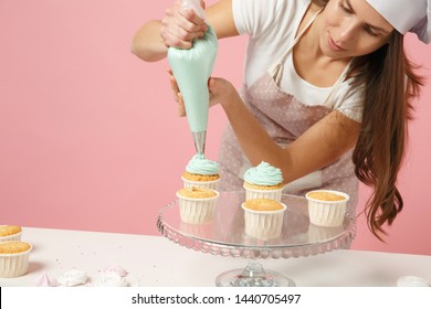 Housewife Female Chef Cook Confectioner Or Baker In Apron White T-shirt, Toque Chefs Hat Decorating Cake Cupcake At Table Isolated On Pink Pastel Background In Studio. Mock Up Copy Space Food Concept