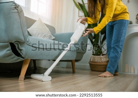 Housewife female dust cleaning floor under sofa or couch furniture with vacuum cleaner, Happy Asian young woman with accumulator vacuum cleaner at home in living room, household and housework concept